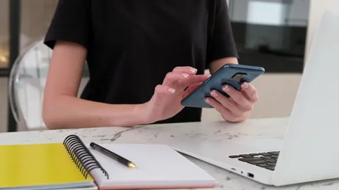 Close-up of a woman using a smartphone while sitting at the table in the kitchen Stock Footage 253407107