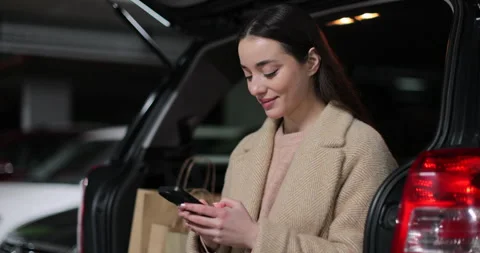 Close-up woman using a smartphone while sitting in the trunk of a car Stock Footage 297755099