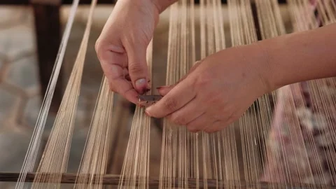 Close-up of a woman weaving silk threads on a classic wooden loom, highlighting Stock Footage 323100943