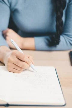Close up of woman writing math notes in notebook at desk with smartphone an.. Stock Photos