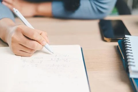 Close up of woman writing math notes in notebook at desk with smartphone an.. Stock Photos