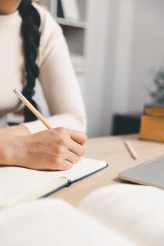 Close up of woman writing notes in notebook beside laptop and open book at .. Stock Photos