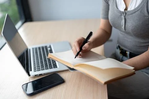 Close Up of Woman Writing Notes In Notebook Beside Laptop At Desk Stock Photos