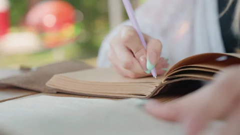 Close up of woman writing in open notebook with purple pen soft focus outdoor Stock Footage 345132568