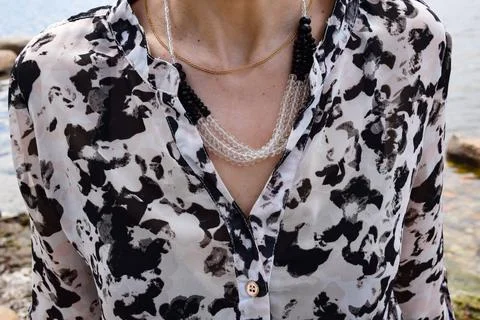 Close-up of a woman's chest wearing a patterned blouse and necklaces accessories Stock Photos