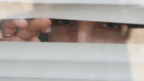 Close-up of a woman's eye looking out into the gap from the blinds. Looking Stock Footage 129255020