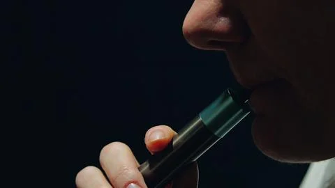 Close-up of a woman's face on a black background with a vape in her lips. A w Stock Photos