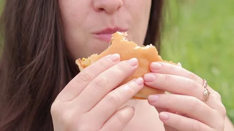 Close-up woman's face eats a cheeseburger in nature Video stock 241783775