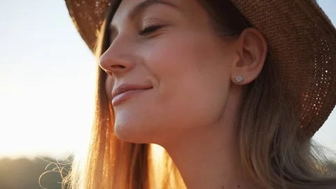 Close up of woman's face with hat smile feel happy outside at sunrise sunset Stock Footage 94271316