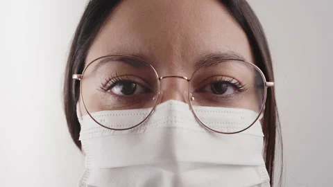 Close-up of a woman's face with mask and glasses looking at a serious camera  Stock Footage 148349722