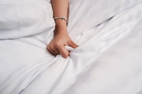 Close up of a woman's hand clenching and gripping the white bed sheet, havi.. Foto stock