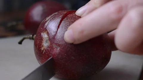 Close-up of a woman's hand cuts a red passionfruit with a knife in the middle Stock Footage 151752438