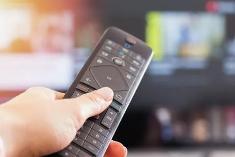 Close-up of woman's hand holding remote control in front of TV, Stock Photos