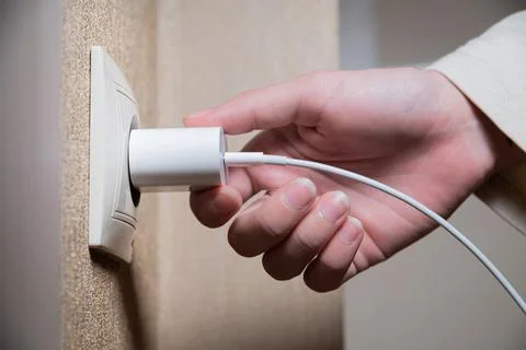 Close-up of a woman's hand inserting a white usb charger into a 220 volt socket Stock Photos
