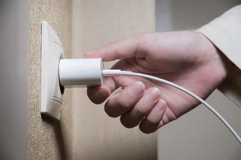 Close-up of a woman's hand inserting a white usb charger into a 220 volt socket Foto stock
