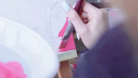 A close-up of a woman's hand paints over a painting with pink acrylic paint in Stock Footage 202576351