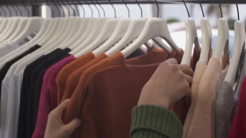 Close-up of woman's hand picking sweater from fashion boutique rack Stock Footage 131675914