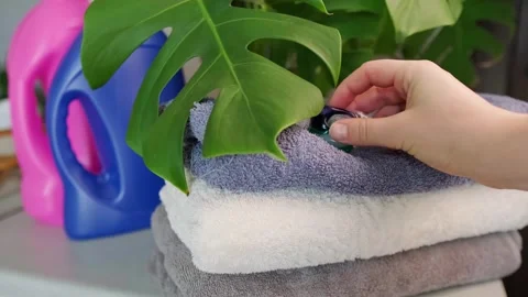 Close-up of a woman's hand placing a detergent capsule on a towel, with bleach a Stock Footage 295285965