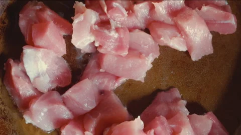 Close-up of woman's hand placing pieces of red meat into frying pan. View f.. Stock Footage 257615480