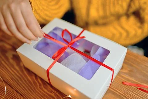 Close-up of woman's hand pulling ribbon from gift box. Stock Photos