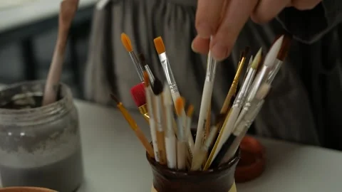 Close-up of a woman's hand putting a paint brush into a vase with other brushes. Stock Footage 272223835