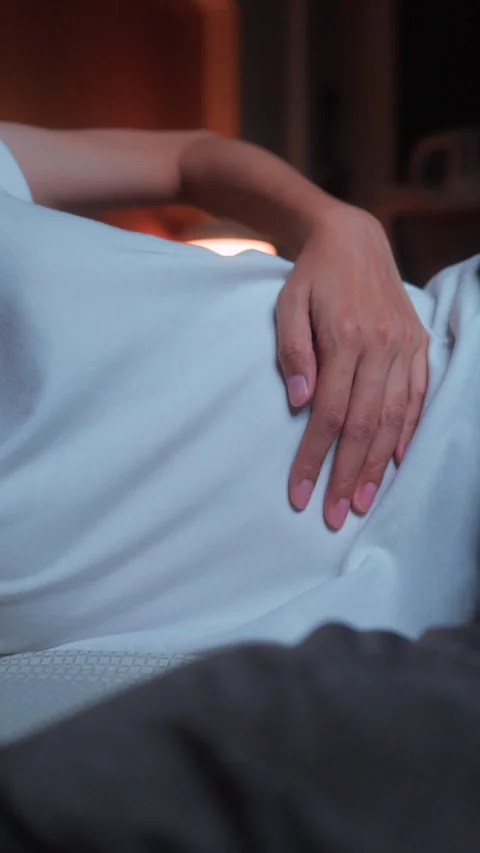 Close-up of a woman's hand resting on her stomach while lying in bed at night Vidéo 347147358
