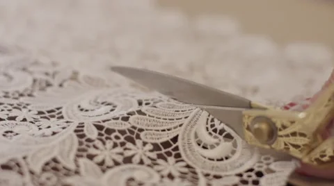 Close-up of a woman's hand with scissors cutting a white lace fabric Stock Footage 61738193