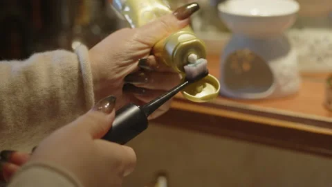 Close up of a woman's hand squeezing toothpaste onto an electric Stock Footage 202887801