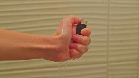 A close-up of a woman's hand tries to light a lighter in the shower under water Stock Footage 202203384