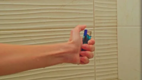 A close-up of a woman's hand tries to light a lighter in the shower under water Stock Footage 202319113