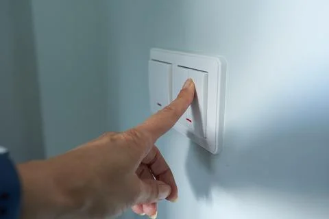 Close-up of a woman's hand turning on a light switch. Stock Photos