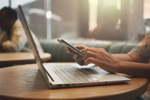 Close-up of woman's hand using smartphone while working on laptop in a coffee Foto stock