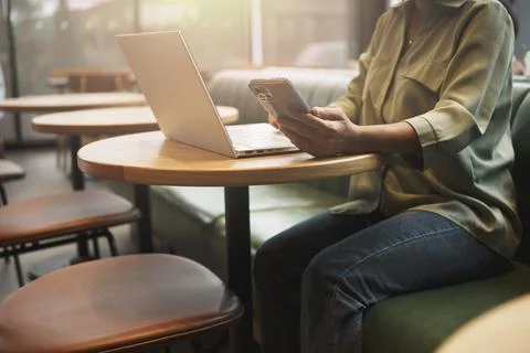 Close-up of woman's hand using smartphone while working on laptop in a coffee Stock Photos