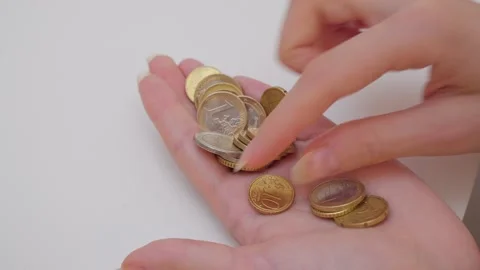 A close-up of a woman's hand on a white background counts yellow euro coins in Stock Footage 203790503