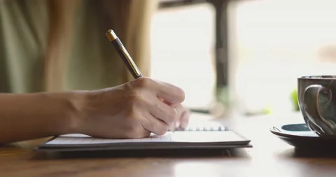 Close up of woman's hand writing down on paper notebook with coffee cup on table Stock Footage 159065089