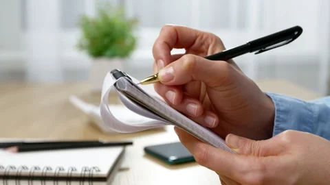Close-up of a woman's hand writing in a notebook on a desk.  Vídeos de archivo 329557497