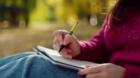 Close-up of a woman's hand writing with a pen in a notebook in an autumn park. Vídeos de archivo 259016465