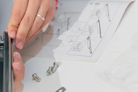 Close-up of a woman's hands assembling a metal part while following instructions Stock Photos