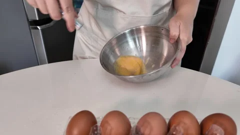 Close-up of a womans hands beating eggs in a metal bowl on a table, kitchen Stock Footage 319341532