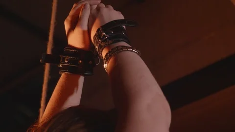 Close up of woman's hands in black leather handcuffs tied to plank in room Stock Footage 118643052