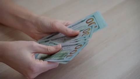 Close-up of a woman's hands counting a stack of dollars on a wooden table Stock Footage 257394300