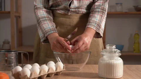 A close-up of a woman's hands cracking an egg with a knife over a clear gla.. Stock Footage 338396671