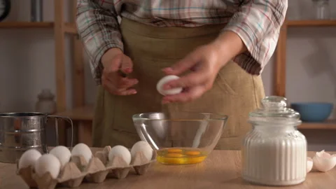 A close-up of a woman's hands cracking an egg with a knife over a clear gla.. Stock Footage 338396845