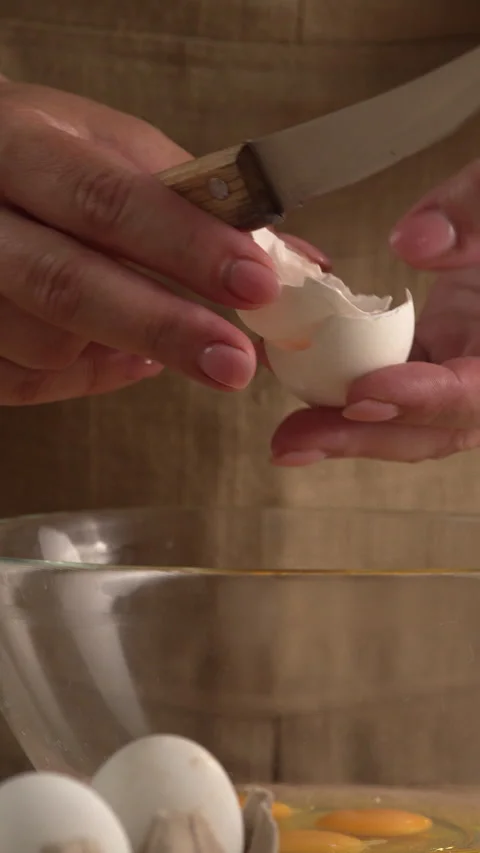 A close-up of a woman's hands cracking an egg with a knife over a clear gla.. Stock Footage 338397253