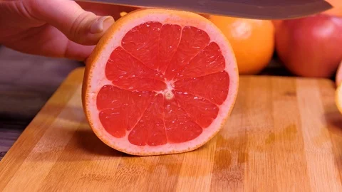 Close up. Woman's hands cutting fresh grapefruit on kitchen Stock Footage 123356444