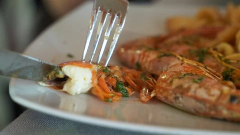 Close-up of woman's hands cutting grilled king shrimps on the plate with fork Video stock 116129854