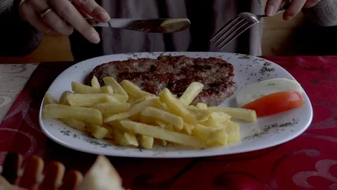 Close up of woman's hands cutting meat dish on plate in restaurant. Stock Footage 96347009