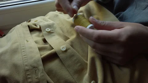 Close up of woman's hands cutting thread, preparing to sew button to yellow shir Stock-Footage 137276441