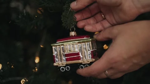 Close-up of woman's hands decorating Christmas tree with toy of retro tram Stock Footage 166545773