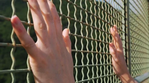 Close-up of a woman's hands gripping an iron mesh overlooking a precipice Stockbeeldmateriaal 265177690
